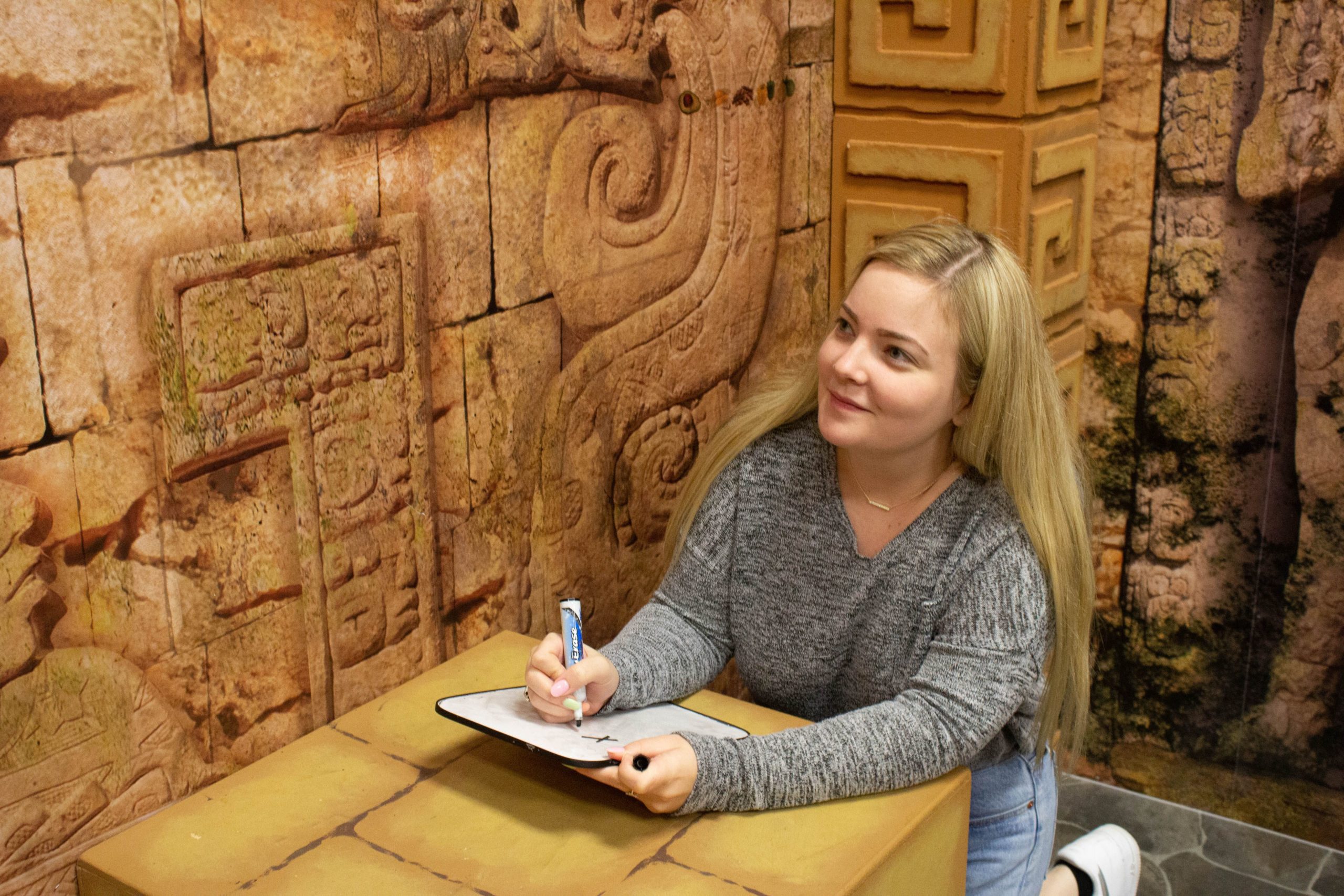 Woman, participating in tomb of the red queen escape from taking notes to solve puzzle